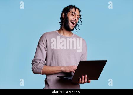 Happy arab man holding laptop and having fun communication in video call. Smiling person with cheerful facial expression holding portable computer and talking in online meeting Stock Photo