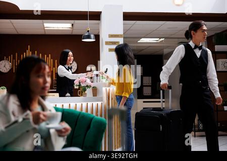 Visitor getting card key from Asian receptionist in contemporary hotel lobby and is then shown to room. Traveler is assisted by friendly staff upon check in at modern resort Stock Photo