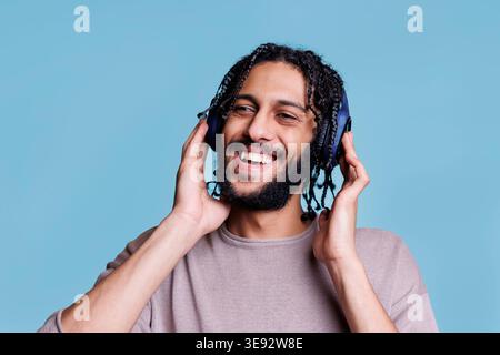 Carefree arab man listening to songs playlist in wireless headphones, smiling and looking away. Happy smiling person enjoying music in earphones, satisfied with sound quality Stock Photo