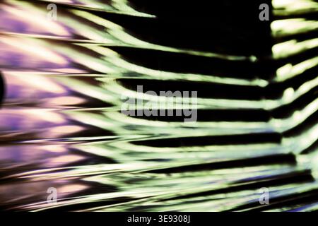 Rippling waves of mint green and pale pink light on a textured dark surface creating a rhythmic pattern Stock Photo
