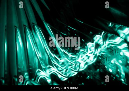 Wavy strands of vibrant teal and turquoise light streaks against a dark textured background Stock Photo