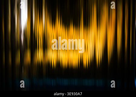 Vertical glowing yellow light streaks forming an abstract shimmering curtain on a black background Stock Photo