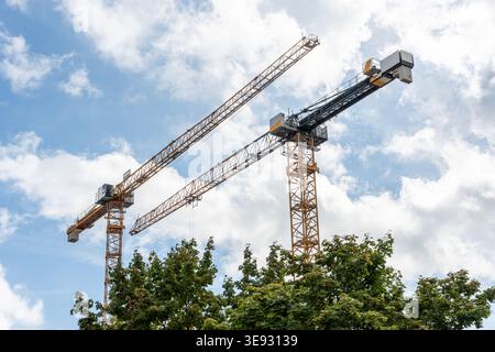 Industrial tower cranes constructing new urban buildings. Showing concepts of development, progress, and city growth under a cloudy sky Stock Photo