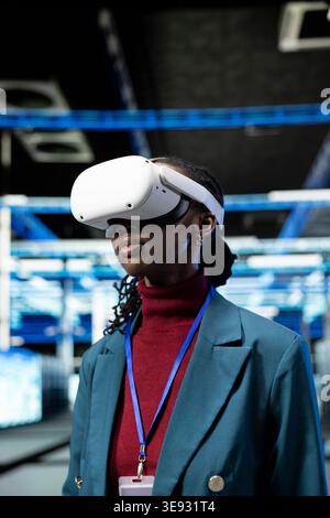 Overseeing supercomputers, VR goggles and technician in data center with large scale IT infrastructure. Using virtual reality technology, network management virtualization and IT expert in server farm Stock Photo