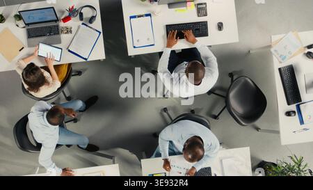 Top down view of diverse colleagues working in modern office, focusing on project planning, performance metrics and report sharing. Business people review data for forecasting. Stock Photo
