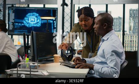 AI startup office personnel automating workflows using neural networks on PC. African american man and team leader refine deep learning models for faster processing, camera B Stock Photo