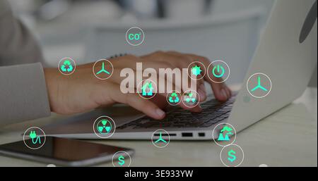 Typing man wearing light long-sleeve shirt on silver laptop at desk, with phone and eco icons Stock Photo