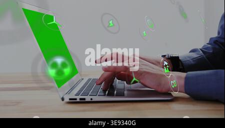 Typing person in blue shirt answering green prompt on laptop at wooden desk, viewing eco icons Stock Photo