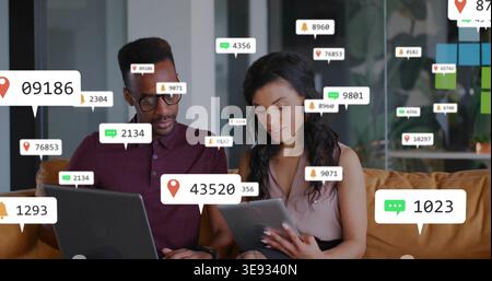 Receiving alerts, coworkers tapping tablet and typing on laptop on sofa, working in office attire Stock Photo