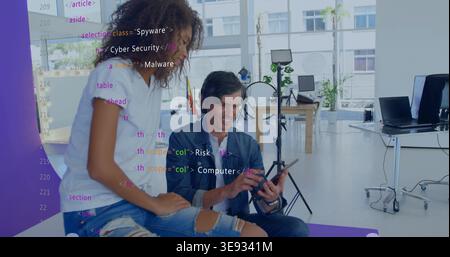 Reviewing code, two coworkers leaning, interacting with tablet in studio in white top, denim jacket Stock Photo