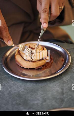 Cutting a cinnamon roll on a metal plate Stock Photo