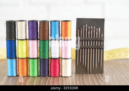 Vibrant rows of colorful sewing thread spools and a needle set on a wood table. Essential supplies for tailoring, embroidery, and DIY craft Stock Photo