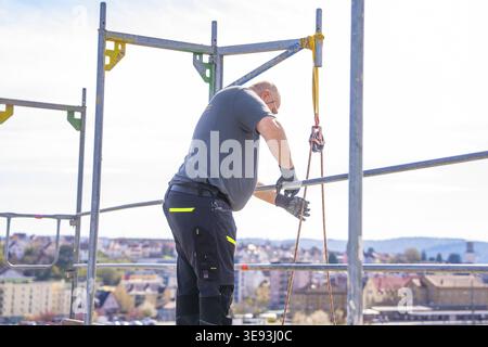 A man in safety clothing on scaffolding. The city and sky are visible in the background, PV Montage. OBI Baumarkt, Muehlacker, Enzkreis, Germany Stock Photo