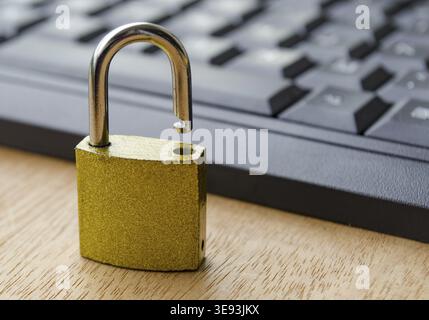 Close up of golden padlock standing next to computer keyboard Stock Photo