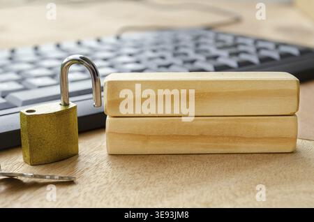 A bright brass padlock positioned on a desk near a computer keyboard with blank wooden blocks with customizable space for text Stock Photo