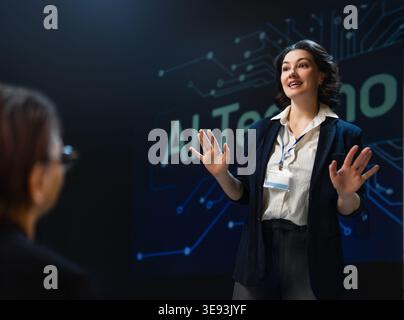 Dynamic businesswoman passionately delivers a presentation on artificial intelligence technology at a professional conference. The engaging public spe Stock Photo