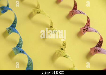 Curled blue, yellow and red measuring tape on vibrant yellow surface represents accuracy and creativity Stock Photo