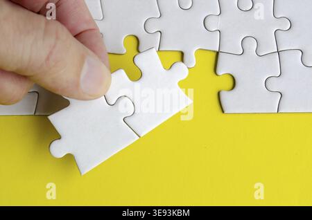 Hand holding jigsaw puzzle pieces on a bright yellow background with customizable space on jigsaw for text or ideas Stock Photo