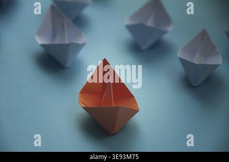 Leadership Concept - Orange color paper ship origami leading the rest of the white paper ship on blue cover background. Copy space Stock Photo