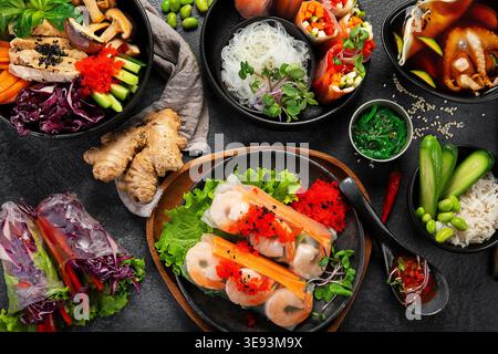Various vietnamese spring rolls filled with various fresh ingredients such as vegetables, spices, meat or shrimps on a dark background. Top view. Stock Photo