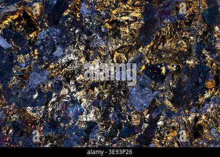 Goldspeckled rock closeup with shimmering highlights, layered crystalline formations and deep indigo tones evoke cosmic terrain, ideal for scifi backg Stock Photo