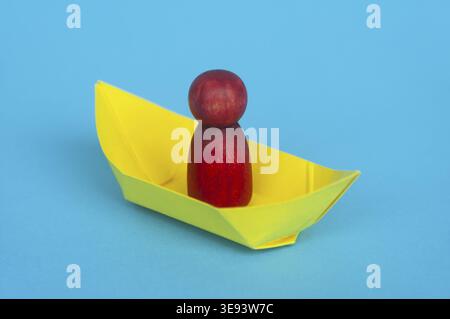 Red wooden figure on yellow paper ship with blue background. Copy space Stock Photo