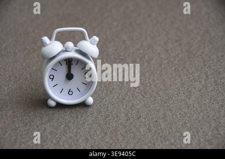 White alarm clock isolated on marble floor The clock set at 12 o'clock. Deadline concept Stock Photo
