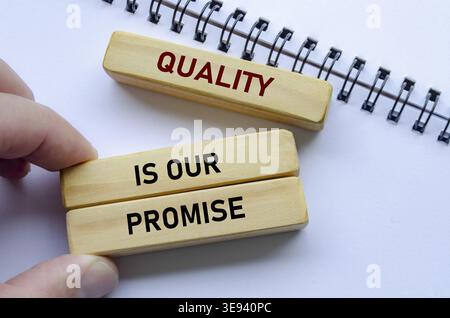 Quality Is Our Promise text on wooden blocks over notebook conveys commitment backed by meaningful intent Stock Photo