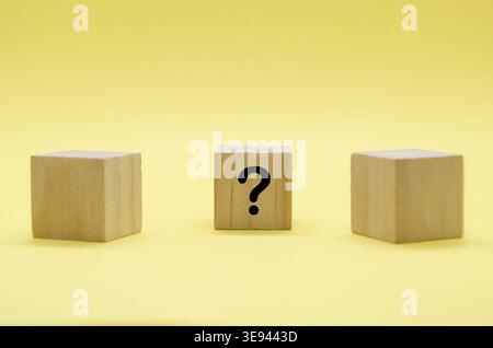 Three light wooden blocks with question marks on pale surface with yellow backdrop Stock Photo