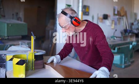 Carpenter sanding wood in a workshop wearing safety gear Stock Photo