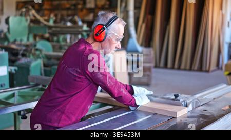Carpenter cutting wood on a wood squaring machine in workshop Stock Photo