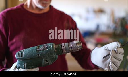 Artisan wearing gloves inserting drill bit into power tool Stock Photo