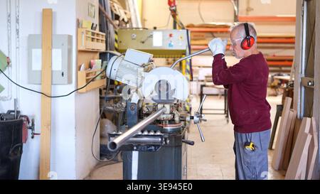 Senior worker cutting metal pipe in workshop with safety equipment Stock Photo