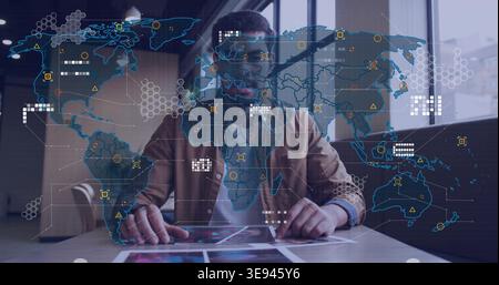 Analyzing tablet and prints, man wearing brown jacket studying global data overlays at office Stock Photo