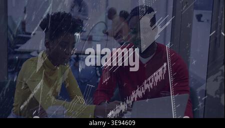 Checking 2 coworkers in yellow top and red sweater reviewing laptop documents in office with charts Stock Photo