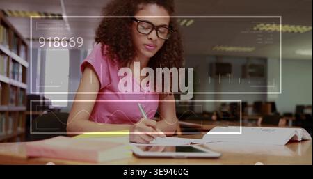 Writing woman wearing pink-shirt glasses at library table, using notebook and tablet HUD overlay Stock Photo