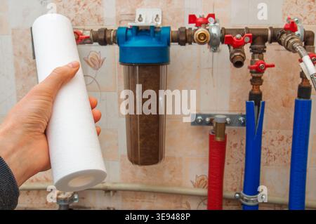 A person's hand holds a clean, white sediment filter cartridge, ready to replace the old, brown, clogged filter in the household water purification sy Stock Photo
