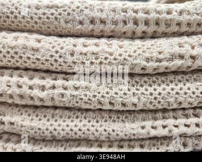 A detailed macro shot showcases the intricate weave and soft texture of stacked beige textile, highlighting its breathable, open-knit structure Stock Photo