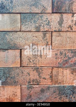 A detailed view of a brick wall showcasing its rough texture, aged patina, and a blend of earthy colors like terracotta and slate blue Stock Photo