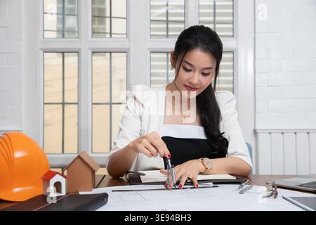 Female architect using dividers working on blueprint architects project in office. Stock Photo