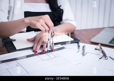 Female architect using dividers working on blueprint architects project in office. Stock Photo