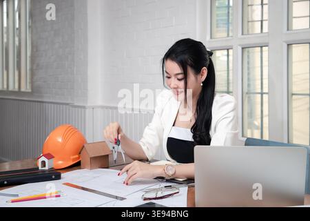 Female architect using dividers working on blueprint architects project in office. Stock Photo