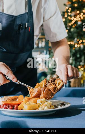 A man is serving food on a plate. The plate has a variety of food items, including meat, vegetables, and potatoes. The man is using a fork to serve th Stock Photo