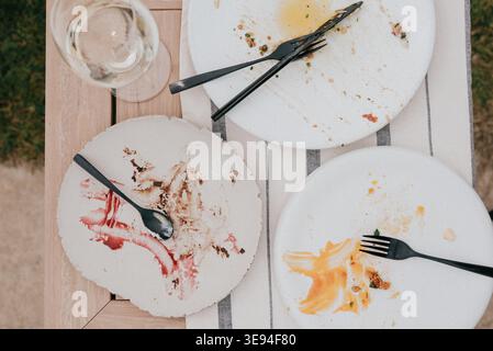 Three plates show leftover food traces after a meal. Forks and spoons lie scattered on white plates. Glass of water sits beside the table setting. Out Stock Photo