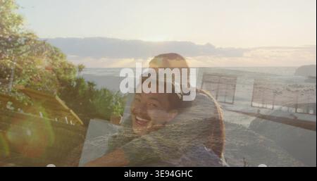 Hugging smiling Asian man while woman embracing on coastal deck, showing cushions and lens flare Stock Photo
