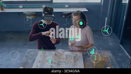 Examining maroon-sweater and pink-blouse designers in studio using VR headset tablet model AR icons Stock Photo