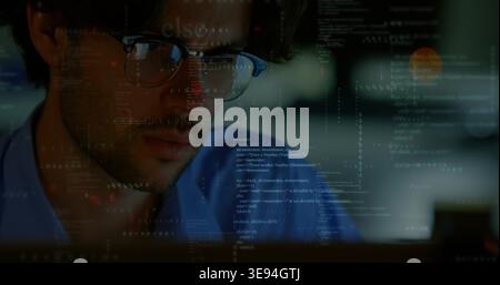 Studying developer focusing on code at dim workstation, wearing blue shirt, glasses reflecting code Stock Photo