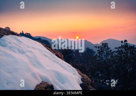 A breathtaking view of the snow-covered landscape at Tungnath temple in Uttarakhand, India, with the sun setting behind the mountains, casting a warm Stock Photo