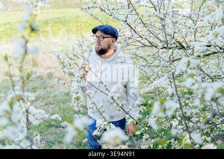 Bearded man among blooming branches in spring garden, calm mindful moment Stock Photo