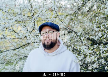 Smiling bearded man in glasses near blooming tree in spring Stock Photo